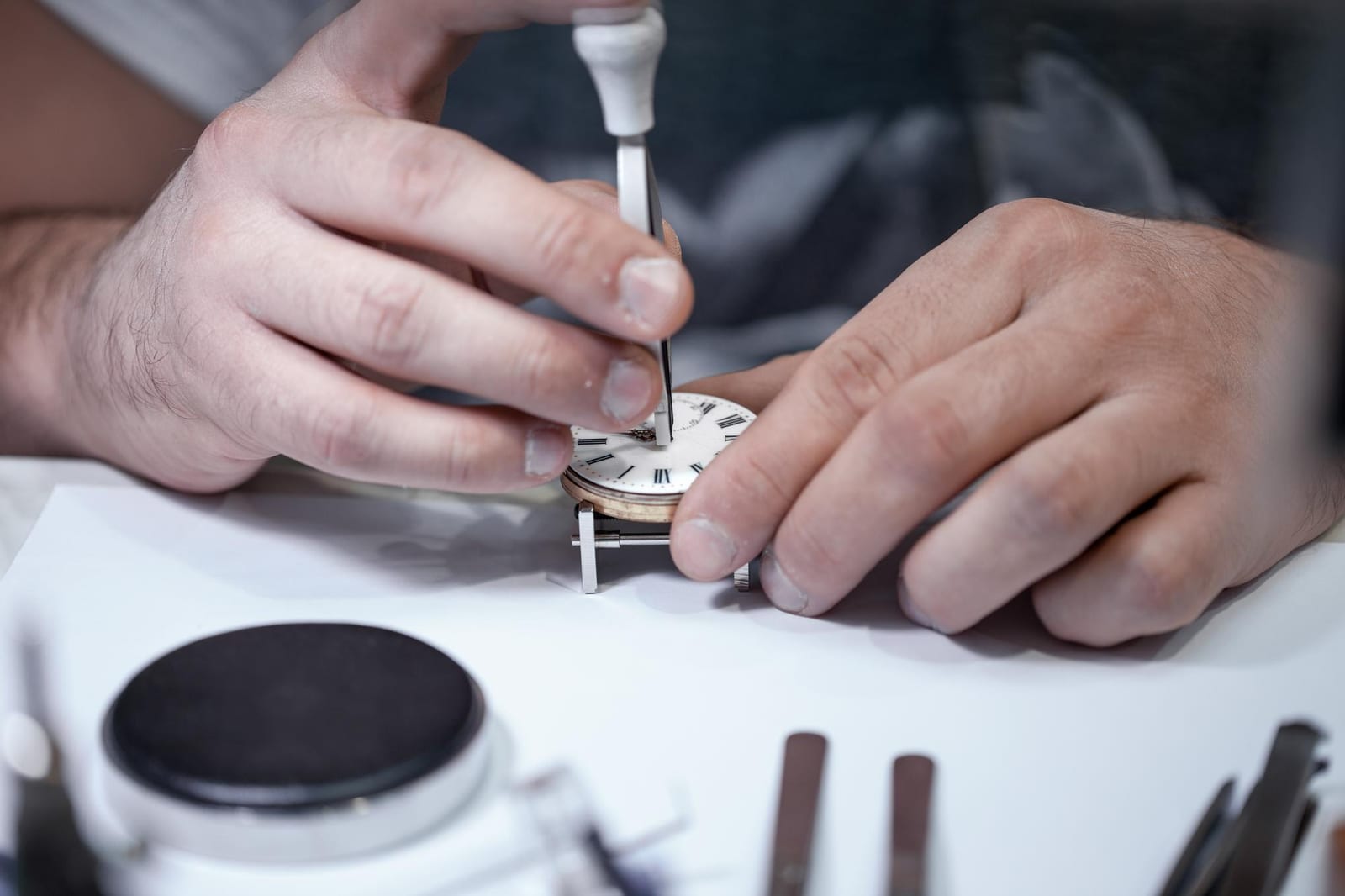 Mani di un orologiaio al lavoro su un quadrante da tasca